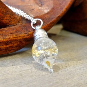 May include: A silver chain necklace with a teardrop-shaped glass pendant filled with gold flakes and a single white feather.