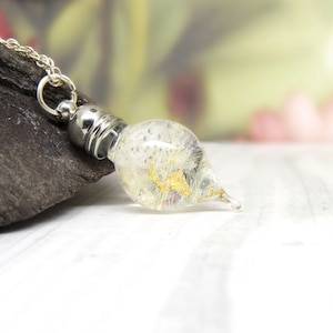 May include: A silver chain necklace with a clear glass teardrop pendant containing gold flakes and iridescent glitter.