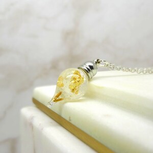 May include: A silver chain necklace with a teardrop-shaped glass pendant filled with gold flakes.