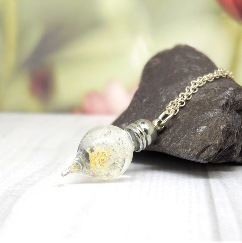 May include: A silver chain necklace with a clear glass pendant containing gold flakes. The pendant is shaped like a teardrop and has a pointed tip.