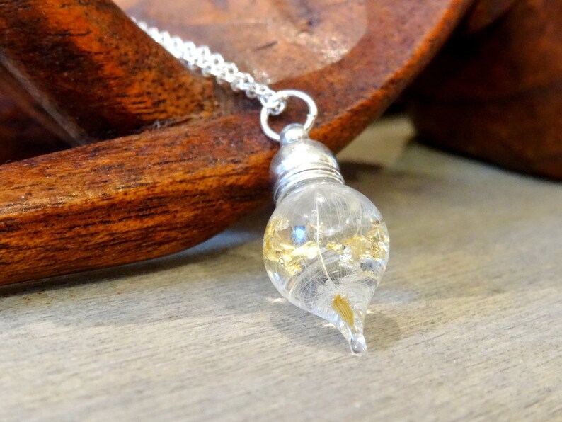 May include: A silver chain necklace with a teardrop-shaped glass pendant filled with gold flakes and a single white feather.