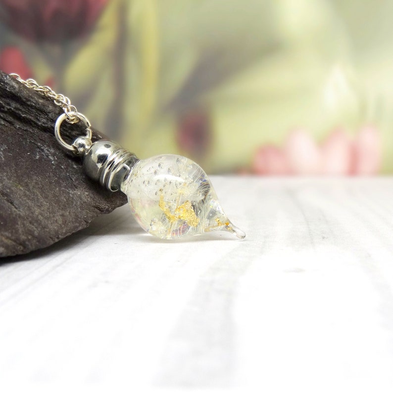 May include: A silver chain necklace with a clear glass teardrop pendant containing gold flakes and iridescent glitter.