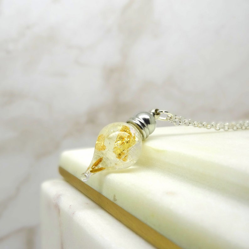 May include: A silver chain necklace with a teardrop-shaped glass pendant filled with gold flakes.