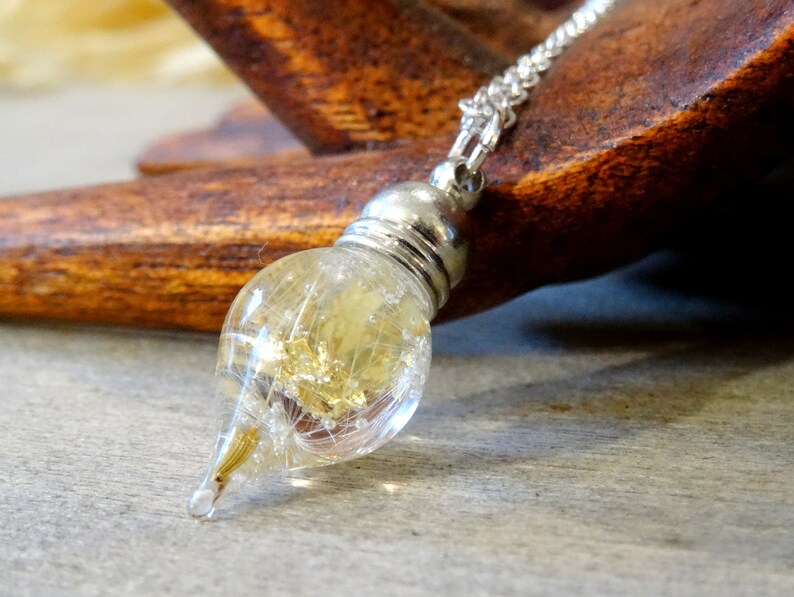 May include: A silver chain necklace with a teardrop-shaped glass pendant filled with dried dandelion seeds and gold flakes.