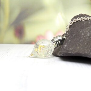 May include: A silver chain necklace with a clear glass pendant containing gold flakes. The pendant is shaped like a teardrop and has a silver cap.