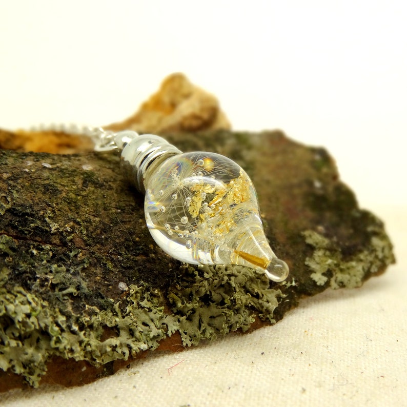 May include: A silver chain dangles from a clear glass pendant filled with gold flakes and dandelion seeds. The pendant is shaped like a teardrop and has a silver cap at the top.