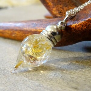 May include: A silver chain necklace with a teardrop-shaped glass pendant filled with gold glitter and white feathers.