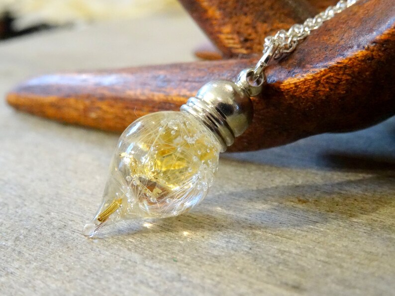 May include: A silver chain necklace with a teardrop-shaped glass pendant filled with gold glitter and white feathers.