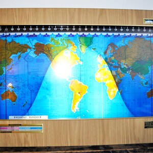 May include: A wooden framed world clock with a blue and yellow map of the world. The clock shows the time zones and the current time. The clock also has a calendar with the months of November and December.