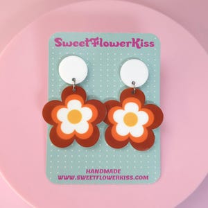May include: A pair of retro-style flower earrings. Each earring features a white circle top and a large flower design with brown, orange, and white layers. The earrings are displayed on a teal card with the text "SweetFlowerKiss" and "HANDMADE www.sweetflowerkiss.com".