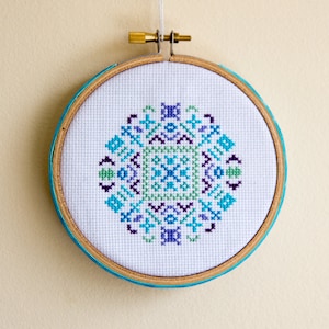 May include: A white embroidery hoop with a blue, green, and purple geometric pattern stitched in the center.