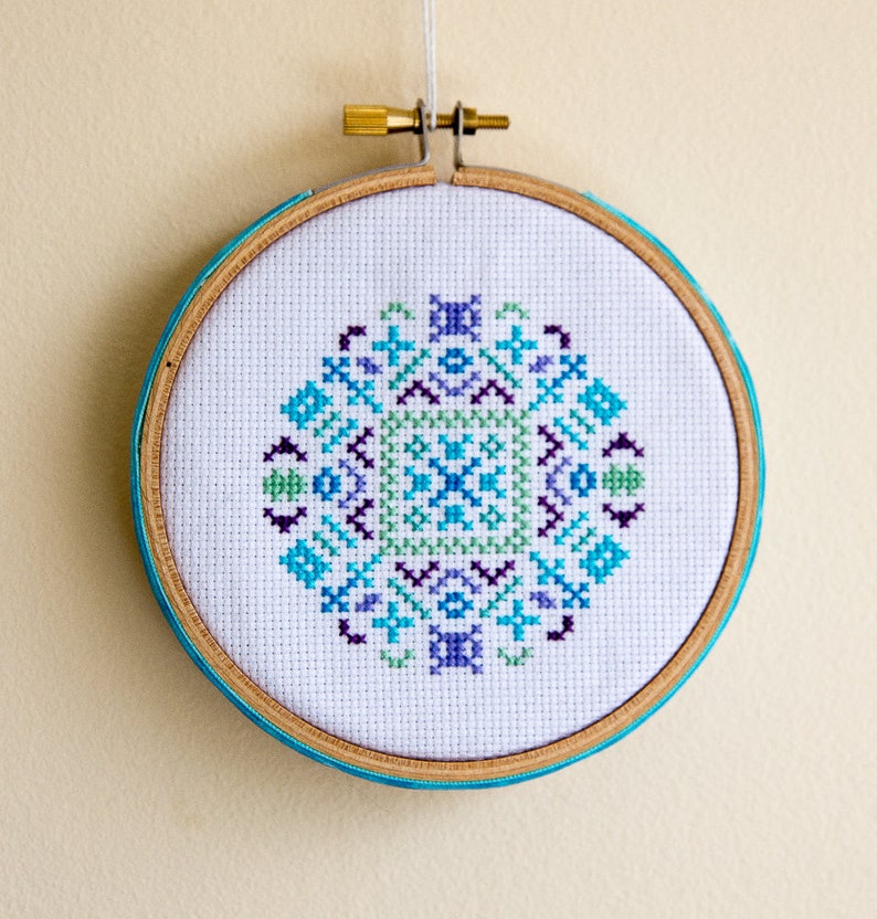 May include: A white embroidery hoop with a blue, green, and purple geometric pattern stitched in the center.