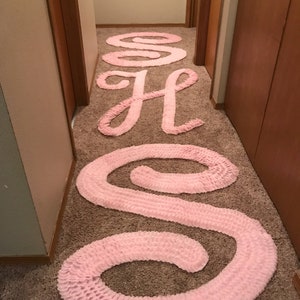 May include: A hallway with a pink fabric rug shaped like the letters "S O S" in a hallway with beige carpet.