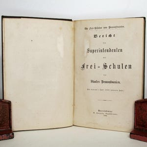 May include: An open antique book with cream-colored pages and black printed text in German. The title page reads: Die Frei-Schulen von Pennsylvanien. Bericht des Superintendenten der Frei-Schulen des Staates Pennsylvanien. Harrisburg: B. Singerly, 1868.