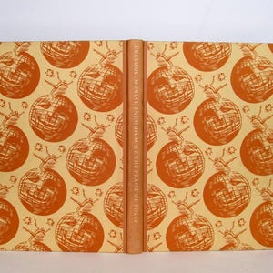 May include: A vintage book with a tan cover and a repeating pattern of orange globes with figures. The spine is a solid tan color with the title "ERASMUS MORIAE ENCOMIUM OR THE PRAISE OF FOLLY" printed vertically.
