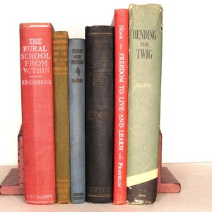 May include: A set of seven vintage hardcover books with red, green, blue, and black spines. The titles include "The Rural School From Within", "Morning Exercise for All the Year", "Fire and Finish", "The Teaching of English", "Freedom to Live and Learn", and "Bending the Twig".
