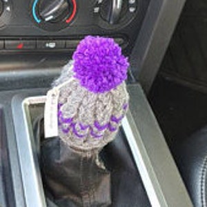 K&ouml;nnte beinhalten: Lila und grauer gestrickter Automatik-Schalthebel-Knopfbezug mit einem Bommel oben drauf.