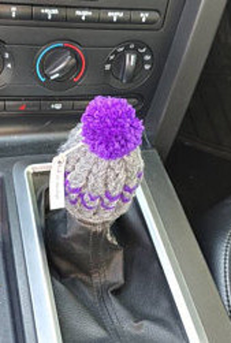 K&ouml;nnte beinhalten: Lila und grauer gestrickter Automatik-Schalthebel-Knopfbezug mit einem Bommel oben drauf.