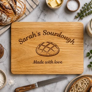 May include: Wooden cutting board with the text "Sarah's Sourdough" and a bread illustration. The words "Made with love" are also engraved on the board. Other items include bread, butter, salt, and a glass of wine.