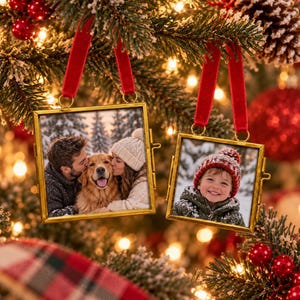 May include: Two square photo ornaments with thin gold metal frames and red velvet ribbon hangers. One ornament displays a couple kissing a golden retriever in the snow, while the other shows a smiling child wearing a red knit hat in a snowy setting.