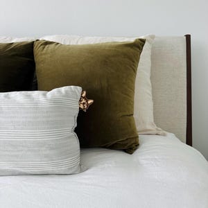 May include: A white bed with a green velvet pillow and a striped pillow. The headboard is brown wood and the bed is made with white sheets.