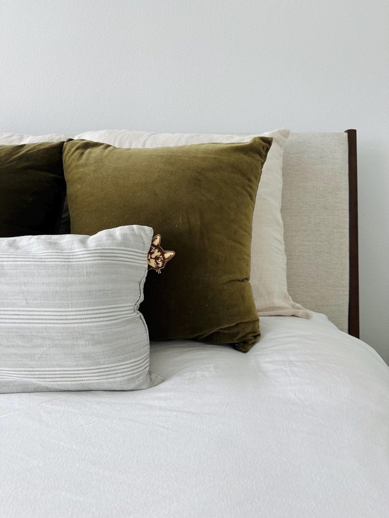 May include: A white bed with a green velvet pillow and a striped pillow. The headboard is brown wood and the bed is made with white sheets.