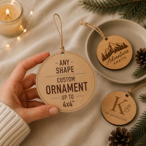 Può includere: Ornamenti in legno personalizzati con cordini. Un ornamento recita "- ANY - SHAPE CUSTOM ORNAMENT FINO A 10x10cm". Altri ornamenti presentano disegni di montagne e iniziali. Una candela accesa e pigne sullo sfondo.