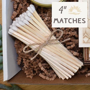 May include: A bundle of 4-inch matches with white tips, tied with twine, presented in a gift box. The matches are displayed on brown crinkle paper. A sign reads "4" MATCHES" with a sun and wave logo.