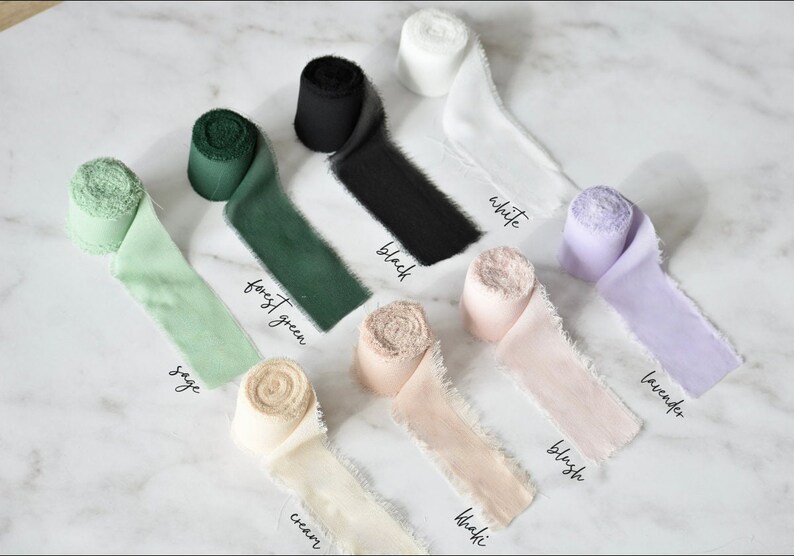 May include: Assortment of silk ribbon rolls in various colors, including sage, forest green, cream, khaki, blush, lavender, white, and black. Each roll is labeled with its color name.