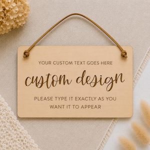 Può includere: Una targa rettangolare in legno chiaro dotata di un cordino in pelle marrone per appenderla. La targa riporta il testo: YOUR CUSTOM TEXT GOES HERE, custom design, e PLEASE TYPE IT EXACTLY AS YOU WANT IT TO APPEAR in caratteri marrone scuro.