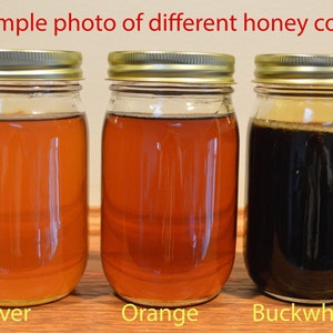 May include: Three glass jars filled with different colored honey. The jars are labeled "Clover", "Orange", and "Buckwheat".
