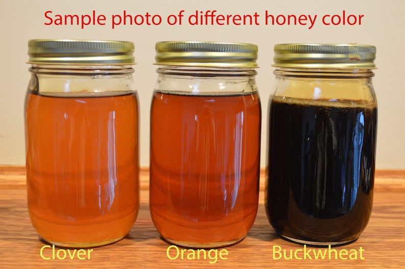 May include: Three glass jars filled with different colored honey. The jars are labeled "Clover", "Orange", and "Buckwheat".