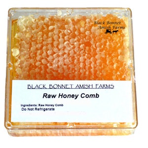 May include: A clear plastic container filled with raw honey comb. The label reads "Black Bonnet Amish Farms Raw Honey Comb" and "Ingredients: Raw Honey Comb Do Not Refrigerate".
