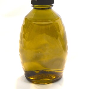 May include: A clear glass bottle with a dark brown, textured surface. The bottle has a black lid and is filled with a light brown liquid.