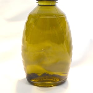 May include: A dark green glass bottle with a black lid, filled with a clear liquid. The bottle has a textured, ribbed design.