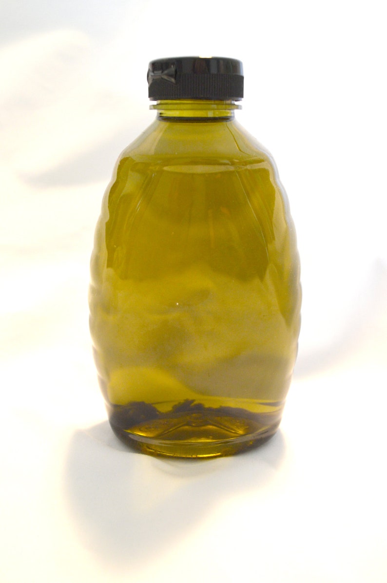 May include: A dark green glass bottle with a black lid, filled with a clear liquid. The bottle has a textured, ribbed design.