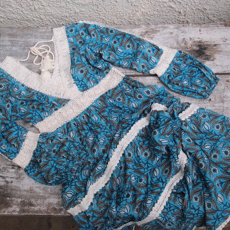 Pode incluir: Um vestido de estampa floral azul e branco com detalhes em croch&ecirc; branco. O vestido tem mangas compridas e decote em V.