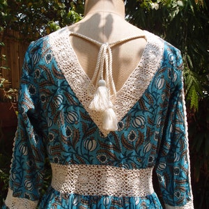 Pode incluir: Um vestido maxi de estampa floral azul e branco com acabamento em renda de croch&ecirc; e um la&ccedil;o de franja branco nas costas.