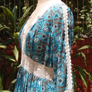 Pode incluir: Um vestido de estampa floral azul e branco com acabamento em croch&ecirc;. O vestido tem decote em V e mangas compridas.