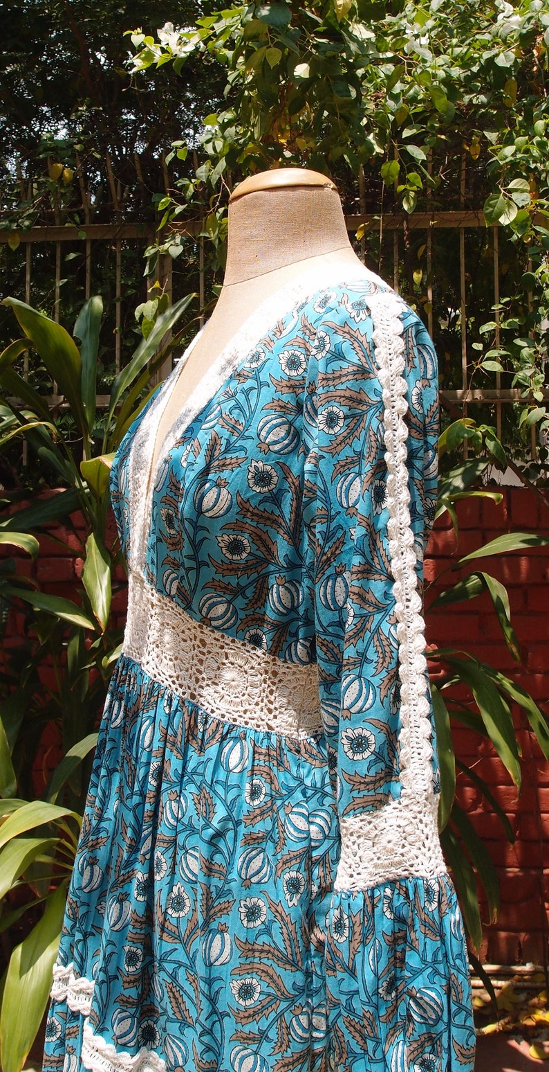 Pode incluir: Um vestido de estampa floral azul e branco com acabamento em croch&ecirc;. O vestido tem decote em V e mangas compridas.