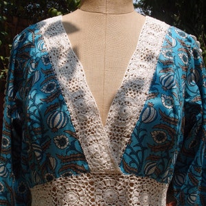 Pode incluir: Um vestido floral azul e branco com uma borda de croch&ecirc; em torno do decote e da cintura. O vestido tem um decote em V e mangas compridas.