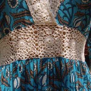 Pode incluir: Um vestido floral azul e branco com um corpete e mangas de croch&ecirc;. O vestido tem um estilo vintage e &eacute; perfeito para um dia de ver&atilde;o.