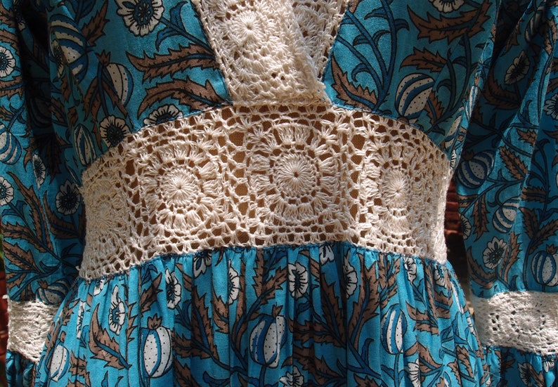 Pode incluir: Um vestido floral azul e branco com um corpete e mangas de croch&ecirc;. O vestido tem um estilo vintage e &eacute; perfeito para um dia de ver&atilde;o.
