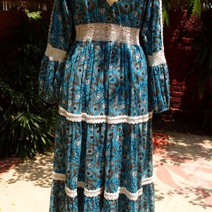Pode incluir: Um vestido maxi floral azul e branco com acabamento em croch&ecirc; e um la&ccedil;o de borla nas costas.