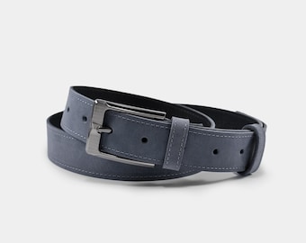 May include: A blue suede belt with a silver-tone buckle. The belt has white stitching along the edges and a matching belt loop. The buckle is rectangular and has a brushed metal finish. The belt is rolled up.
