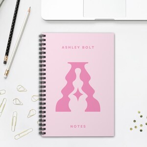 Puede incluir: Cuaderno de espiral rosa con el texto "ASHLEY BOLT" y "NOTES" en la portada. La portada presenta un diseño abstracto rosa de una persona en una postura meditativa.