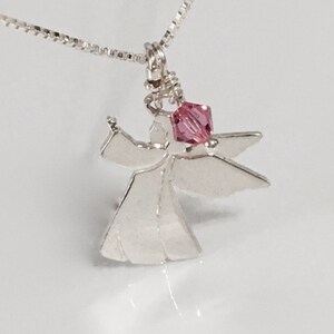 May include: A silver angel pendant necklace with a pink crystal accent. The angel is depicted with outstretched wings and a simple, elegant design.