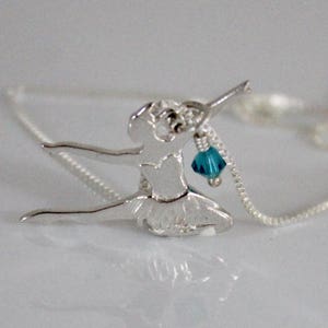 May include: A silver pendant necklace depicting a ballerina in a dance pose. The pendant has a tutu and a teal crystal. The necklace chain is silver. The pendant is likely made of sterling silver.
