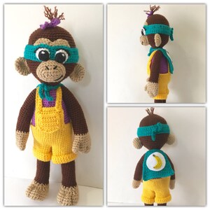 Puede incluir: Un juguete de mono de crochet que lleva un disfraz de superhéroe de color turquesa y morado con un plátano amarillo en la capa. El mono tiene pelo marrón, una diadema morada y grandes ojos marrones.