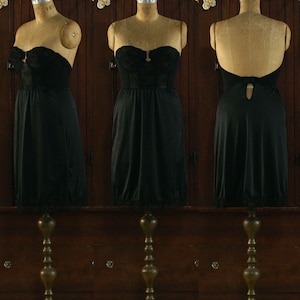 May include: A black strapless slip with lace trim and a keyhole back detail. The slip is displayed on a mannequin against a wooden background.
